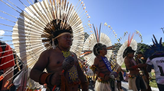 Drei mit grossen runden Federkränzen auf dem Kopf geschmückte Indigene