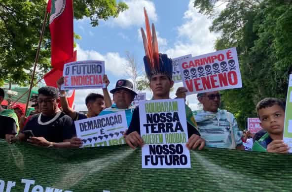 Indigene marschieren in einer Reihe und halten Plakate hoch mit Texten wie: Unser Land ist unsere Zukunft