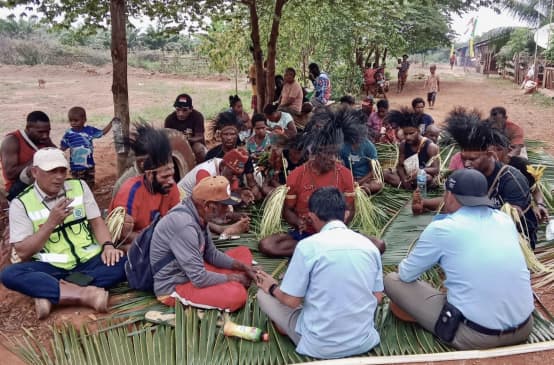 eine Gruppe Papua sitzt auf Palmblättern