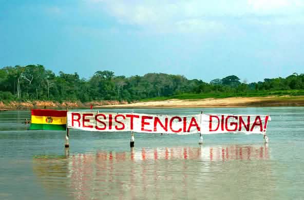 Protestbanner auf einem Fluss im Regenwald von Bolivien: Widerstand bedeutet Würde steht auf dem Banner neben der Flagge Boliviens zu lesen