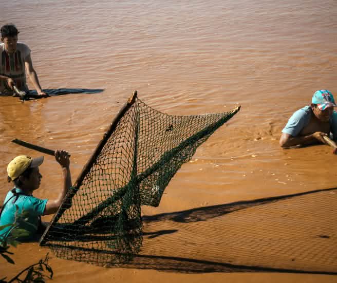 Drei Männer stehen zum Fischfang bis über die Hüften in den braunen Fluten eines Gewässers