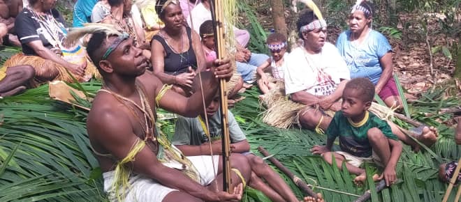 Gruppe Papuas auf Palmblättern sitzend