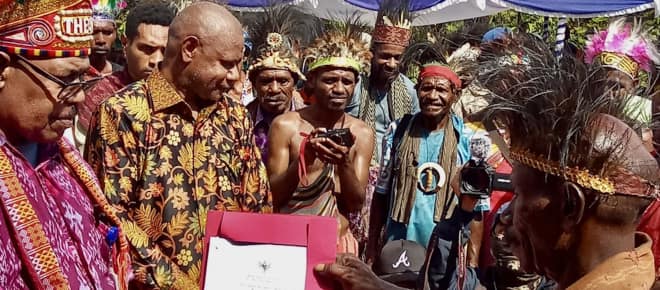 Eine Gruppe Papua in traditioneller Kleidung hält eine Urkunde