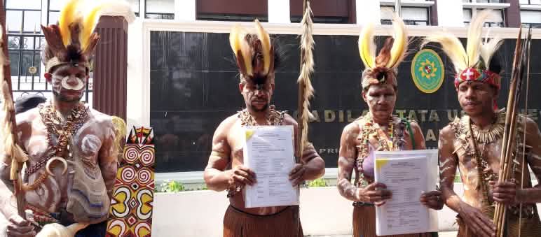 Indigene aus Papua: "Wir gehen in Berufung! Der Prozess entscheidet über die Zukunft des Waldes im Süden Papuas." vier Papua in traditioneller Kleidung vor Gerichtsgebäude