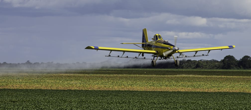 Ein Propellerflugzeug versprüht Pestizide aus der Luft über einem Soja-Feld