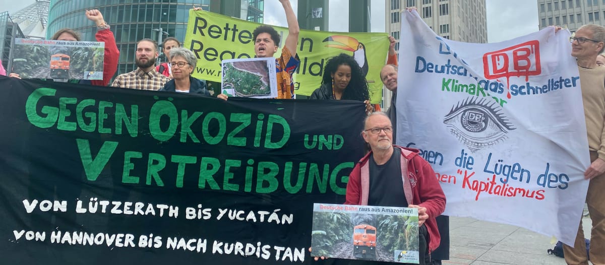 Eine Gruppe von Personen protestiert mit grossen farbigen Bannern vor drei Bürohochhäusern