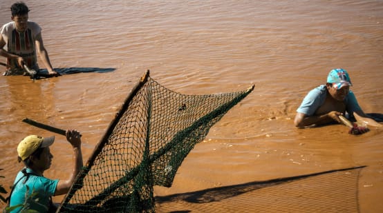 Drei Männer stehen zum Fischfang bis über die Hüften in den braunen Fluten eines Gewässers