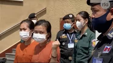 zwei gefangene Frauen in orangener Trauerkleidung, dahinter Polizei