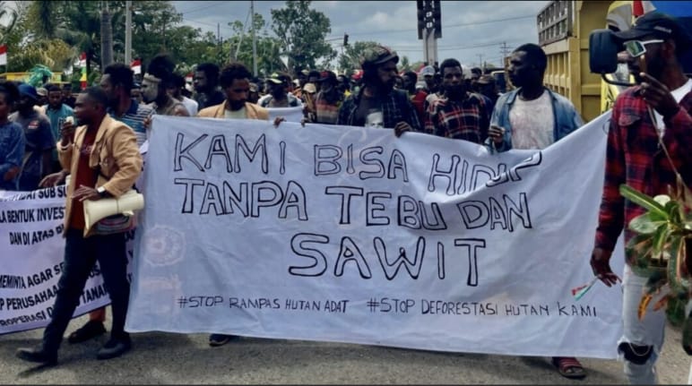 Menschenmenge mit Banner: "Wir können ohne Zucker und Palmöl leben. Stop Raub des Indigenenwaldes. Stop die Abholzung unseres Waldes"