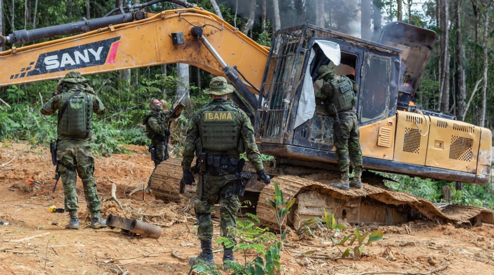 Eine Gruppe von Männern in Tarnanzügen der Umweltbehörde IBAMA zerstört einen gelben Bagger im Regenwald