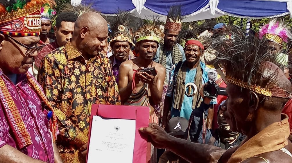 Eine Gruppe Papua in traditioneller Kleidung hält eine Urkunde