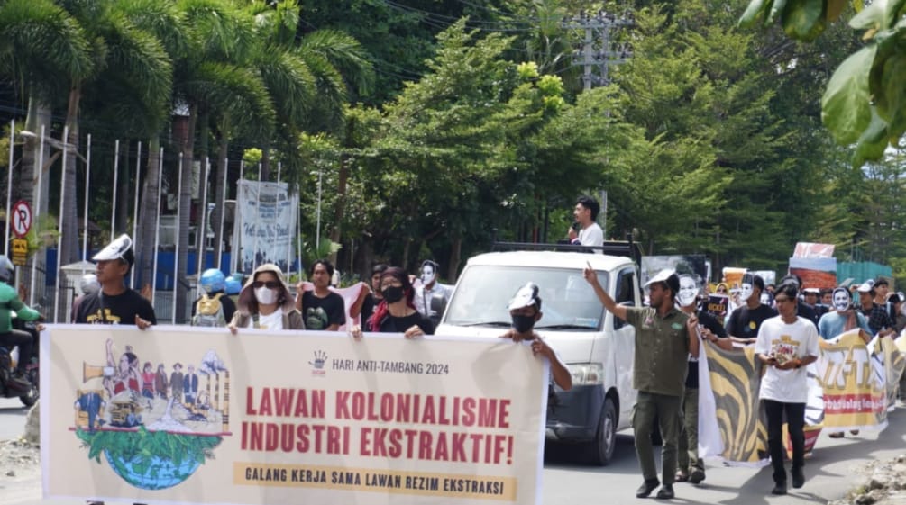 Demo, vorne Banner "Gegen den Kolonialismus der extraktiven Industrien", dahinter Menschen und ein Lastwagen