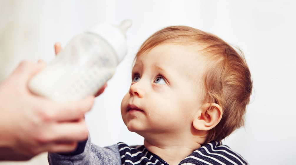 Ein Baby wehrt mit sorgenvollem Blick eine ihm hingehaltene Trinkflasche ab