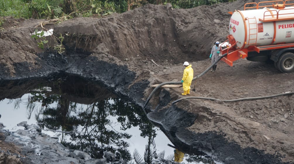 Zwei Ölarbeiter saugen mit einem Schlauch Rohöl aus einem Erdteich in einen Tankwagen