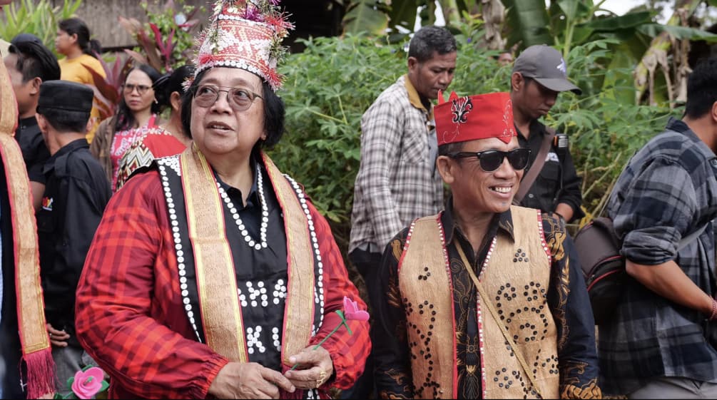 Frau mit roter Jacke und traditioneller Dayak-Kostümierung mit Mann in Weste aus Rinde