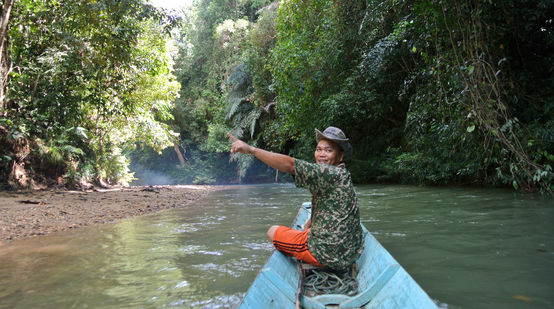 Ein Mann an der Spitze eines kleinen Bootes zeigt begeistert den Regenwald
