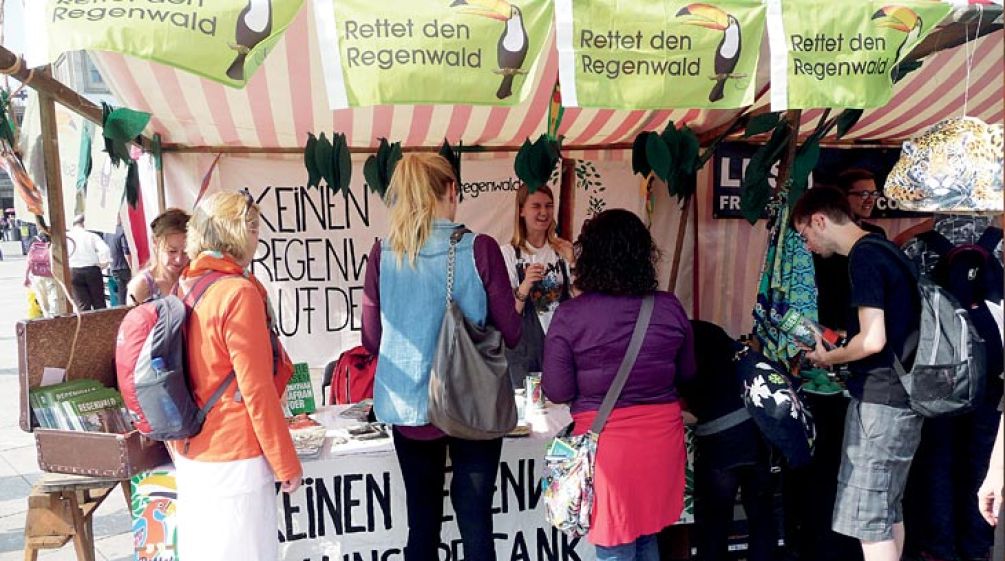 Besucher stehen vor dem bunt-geschmückten Informationsstand von Rettet den Regenwald